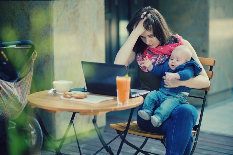 Tired young mother working oh her laptop and holding 4-month son