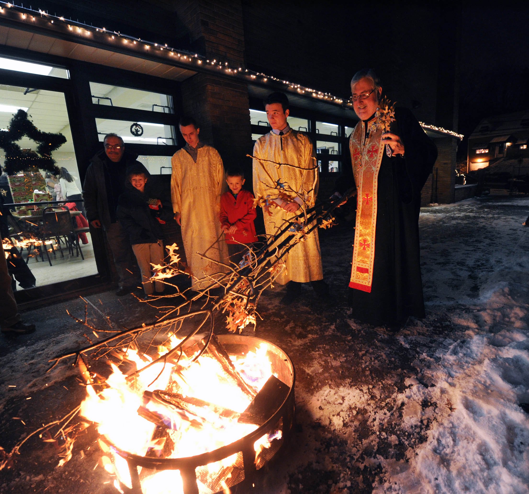 John Heller / Post - Gazette Local / Yule Log McKeesport - Jan. 06, 2014 - Father Stevan Rocknage , right, Pastor of St. Sava Serbian Orthodox Church in McKeesport, oversees the burning of the "Badnjak" or Yule log .The ceremony is usually held out doors but due to extreme cold weather, the Orthodox Christmas Eve service was held in the parish hall under the church. Only the burning of the log was outdoors.